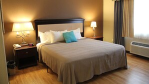 A neatly made bed with a headboard, two bedside tables with lamps, a waste bin, and a window with curtains. - Green Acres Hotel (Pittsfield)