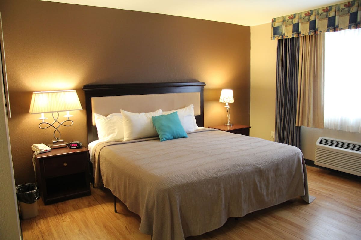 A neatly made bed with a headboard, two bedside tables with lamps, a waste bin, and a window with curtains.