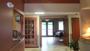 A hotel lobby with a wooden staircase, a ceiling fan, and a dining area in the background. - Green Acres Hotel (Pittsfield)