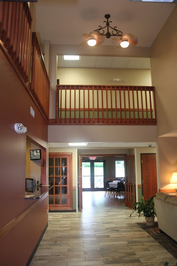 Eine Hotelhalle mit einer Holztreppe, einem Deckenventilator und einem Essbereich im Hintergrund.