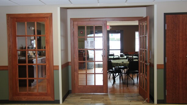 A hallway with wooden doors leading to a dining area with a table and chairs. - Green Acres Hotel (Pittsfield)
