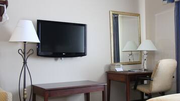 Quarto de hotel com televisão de ecrã plano, secretária com cadeira, candeeiro e cama.