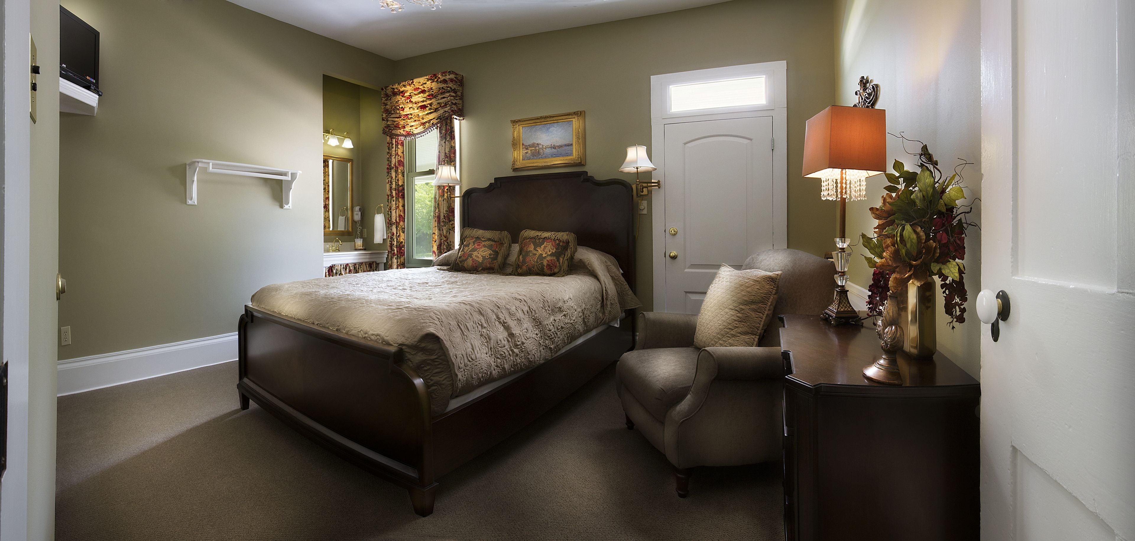 A bedroom with a bed, a chair, a nightstand, a lamp, a door, and a window.