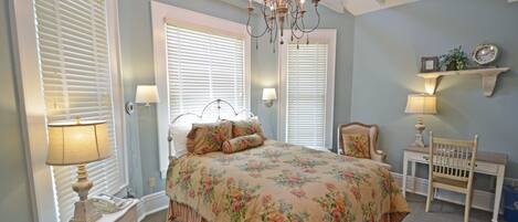 Un dormitorio con colcha estampada, candelabro, mesita de noche con lámpara y una silla.