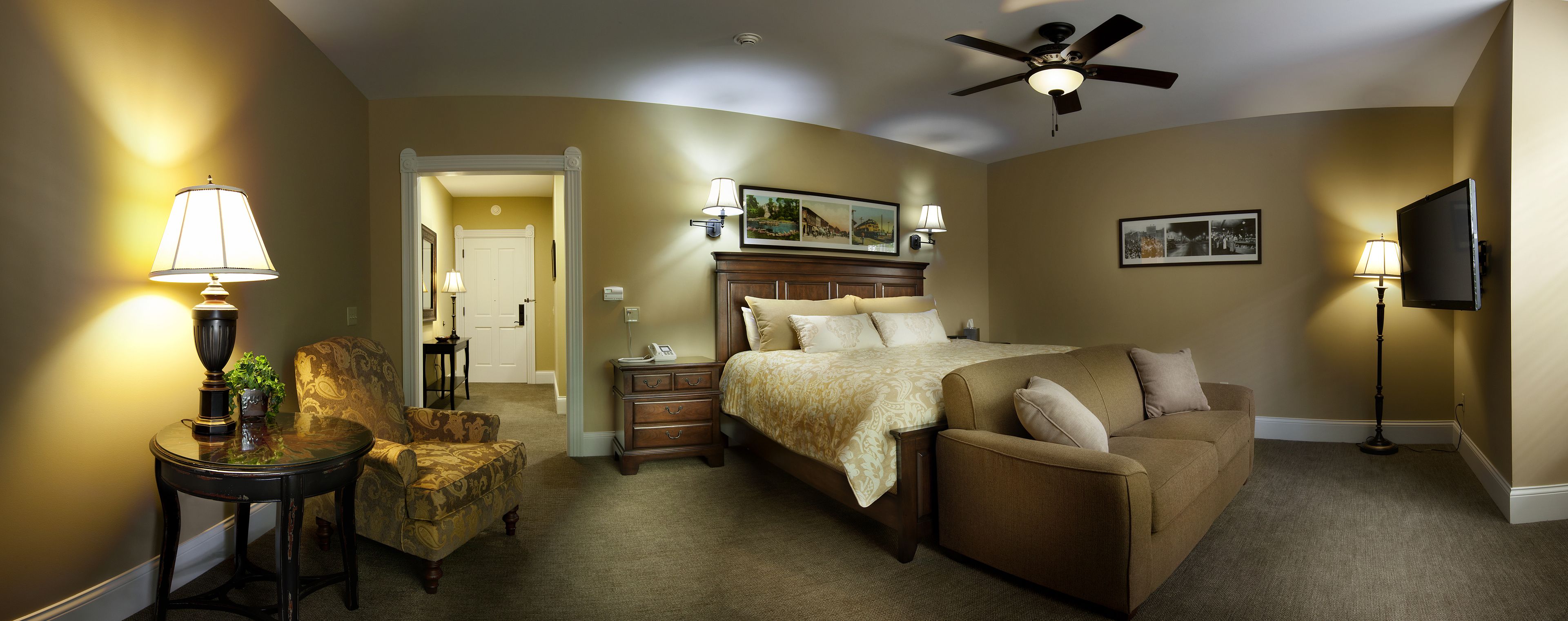 A hotel room with a bed, a sofa, a chair, a desk, and a ceiling fan.