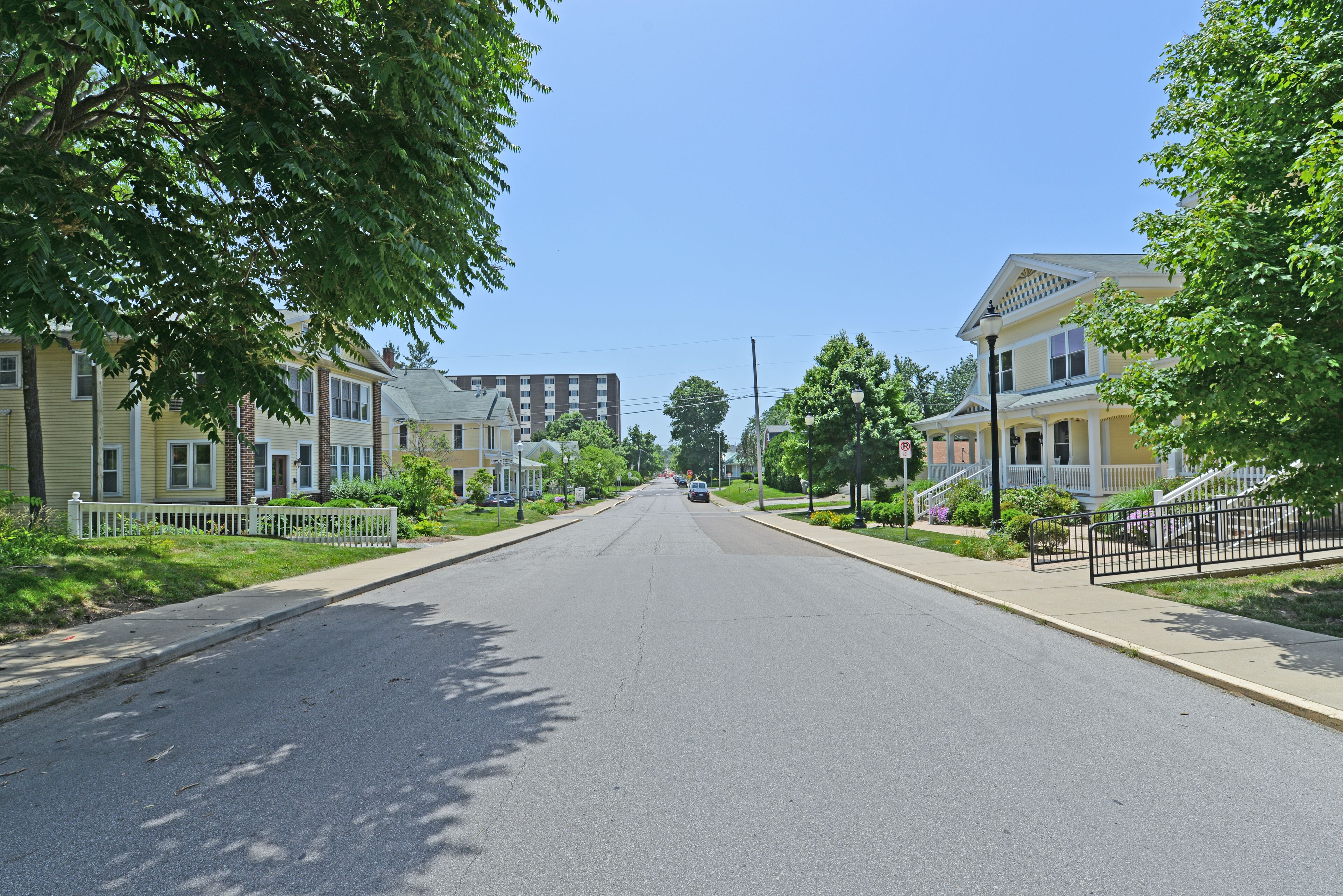 A quiet residential street lined with two-story houses, each with a front porch and a small front yard.