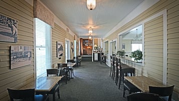 A corridor with wooden paneling, a chandelier, and a dining area with tables and chairs.