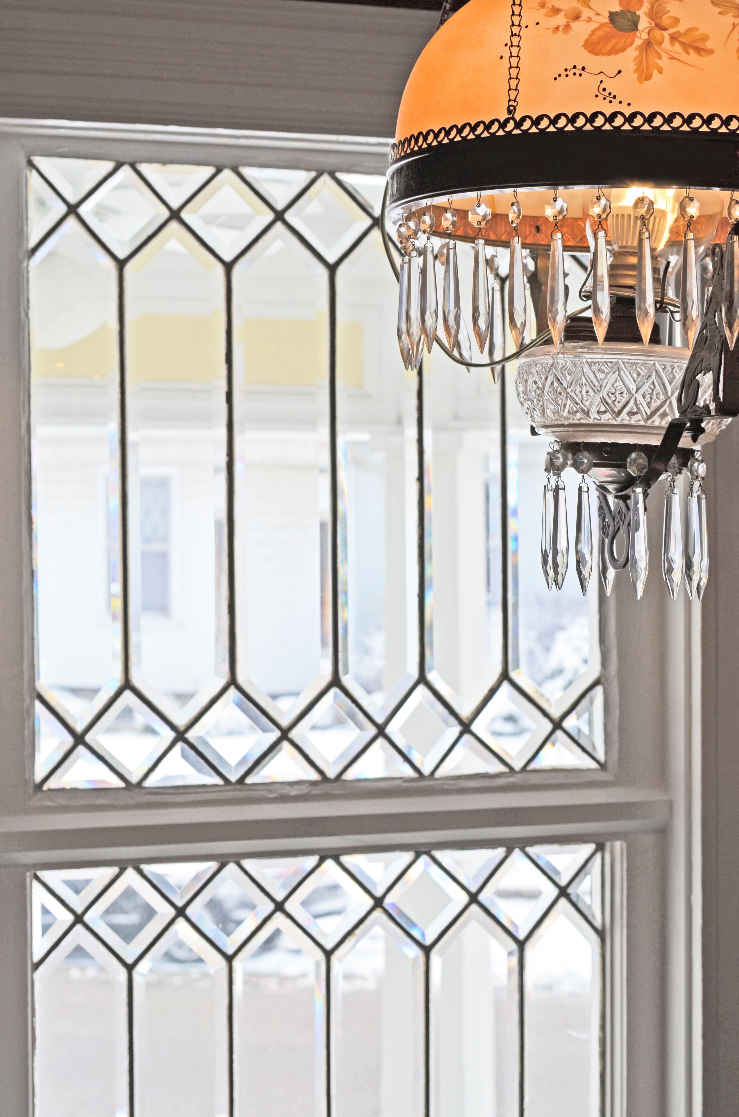 A chandelier with crystal decorations hanging above a window with a diamond-patterned design.