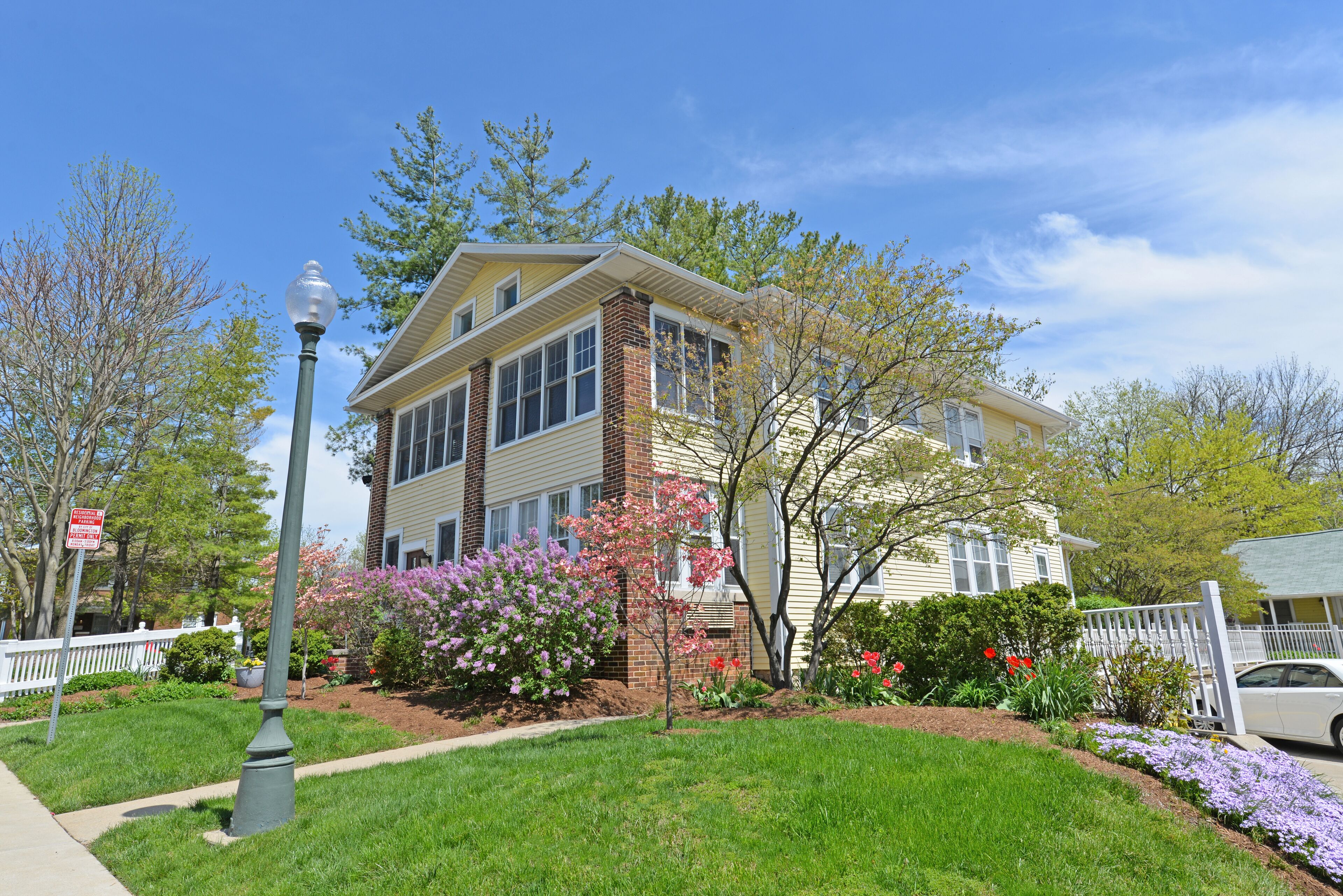 A two-story house with a front yard, a white picket fence, and a street lamp.