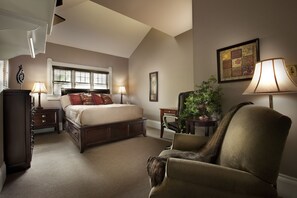 A bedroom with a large bed, two bedside tables, a chair, a desk, a window, and a lamp.