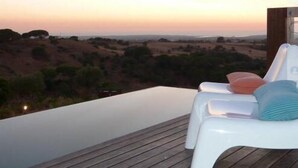 A wooden deck with a pool and lounge chairs overlooking a hilly landscape at sunset. - Eco Suites Resort (Santiago do Cacém)