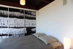 Une chambre à coucher avec un lit, un mur orné d’un tableau abstrait en noir et blanc, et un luminaire au plafond.