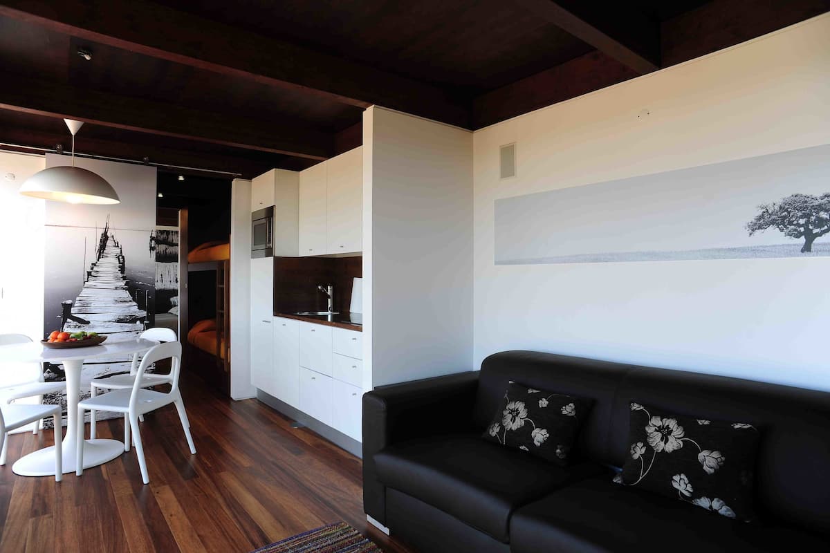 A modern living space with a dining area, a black sofa with floral cushions, and a kitchen in the background.