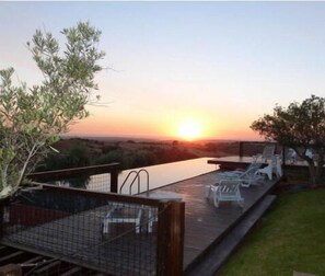 Une vue sur le coucher de soleil depuis une terrasse équipée de chaises longues et d’une piscine.