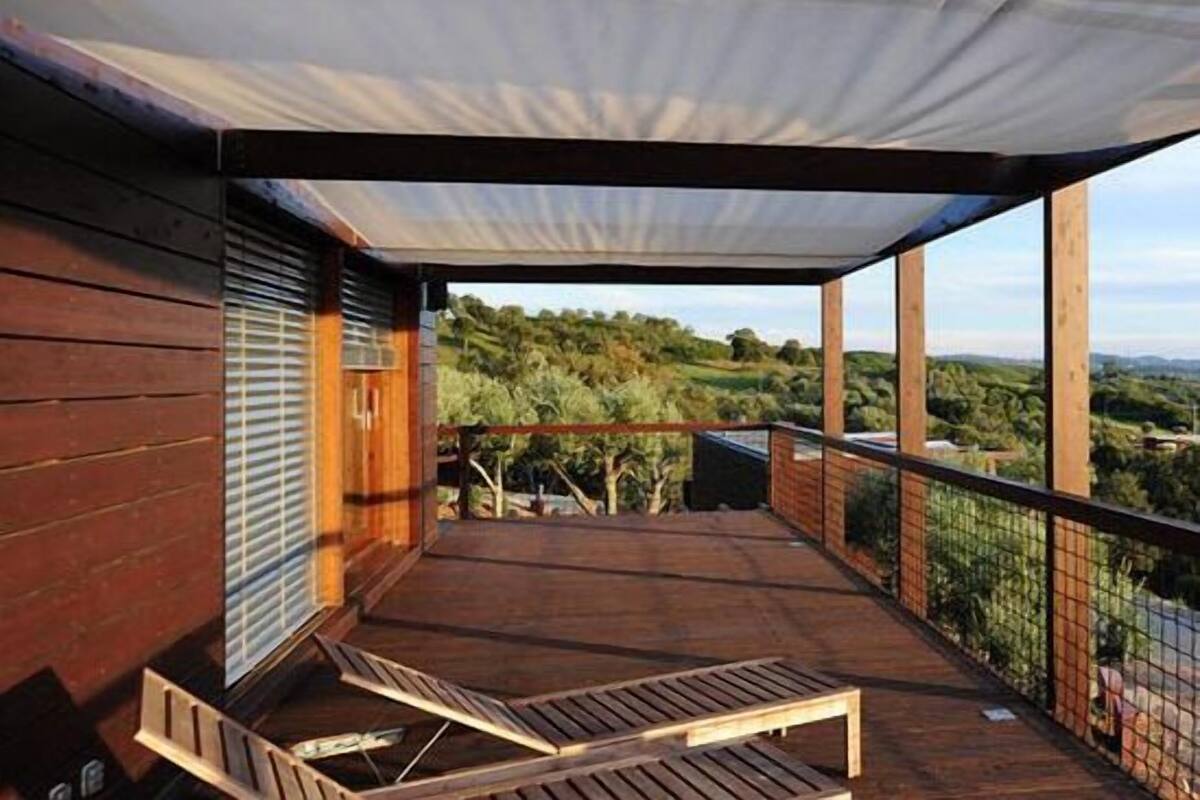 A wooden deck with a covered area, a bench, and a view of a hilly landscape.