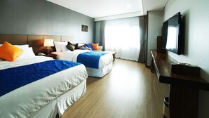A hotel room with two beds, a TV, and a wooden desk.