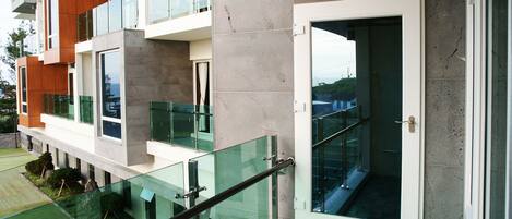 A modern building with a glass balcony, concrete walls, and a metal railing.
