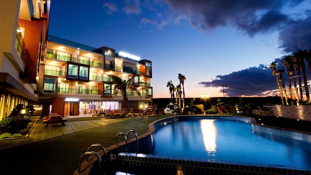 A modern hotel with a swimming pool, multiple balconies, and a well-lit exterior. - Login Resort (Jeju City)
