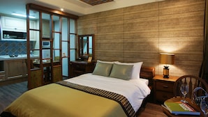 A hotel room with a bed, a nightstand, a lamp, a chair, a dining table, and a kitchen area visible through a glass partition. - Login Resort (Jeju City)