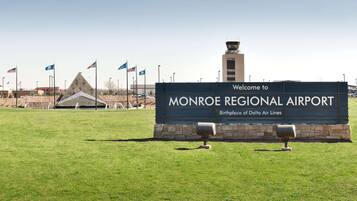 A sign welcoming to Monroe Regional Airport, with flags and a control tower in the background.