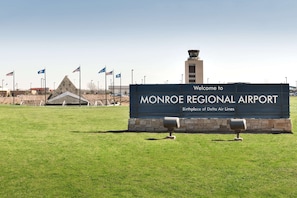 Un panneau d’accueil indiquant l’aéroport régional de Monroe, avec des drapeaux et une tour de contrôle en arrière-plan.