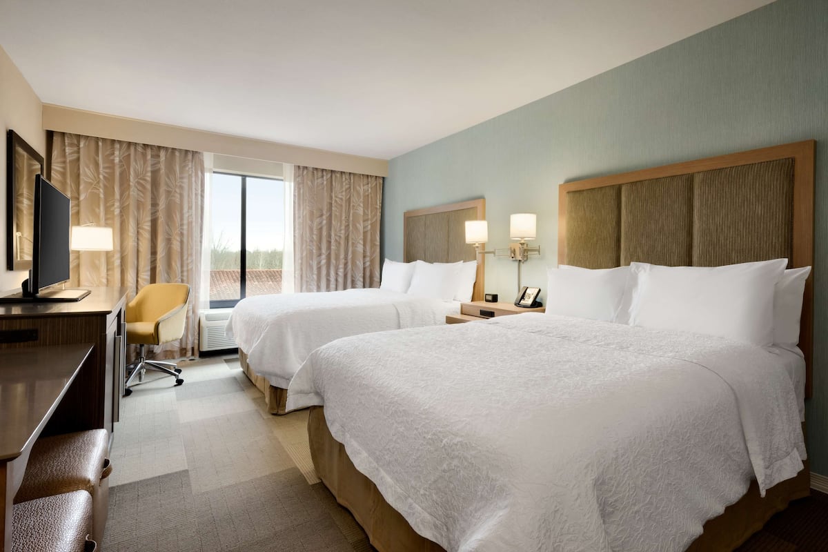A hotel room with two beds, a desk, a chair, and a TV.
