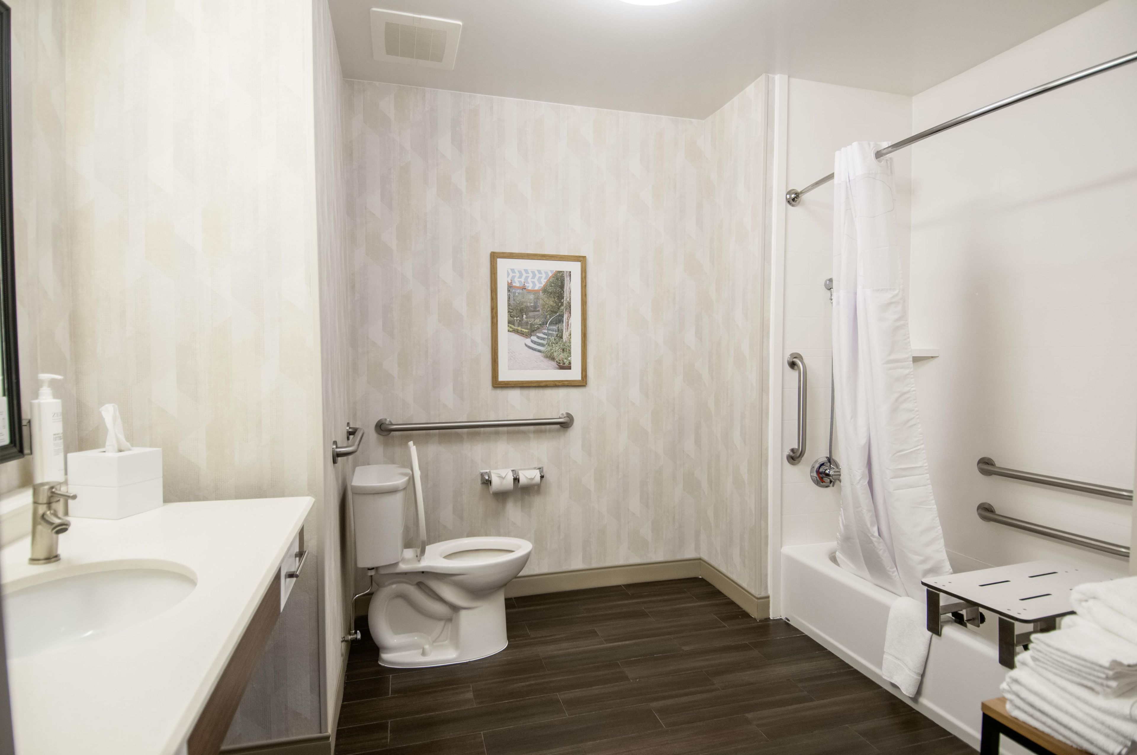 A bathroom with a toilet, bidet, and bathtub. There is a handrail and a picture on the wall.