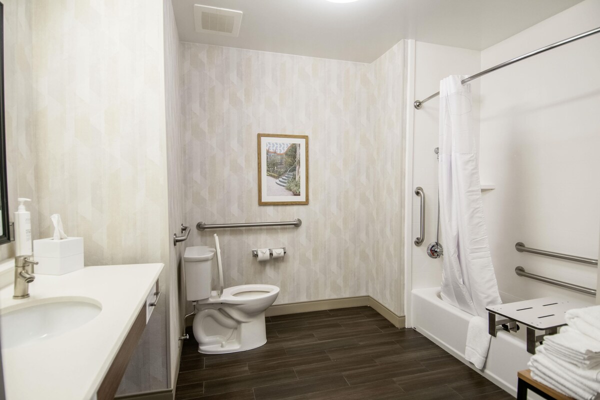 A bathroom with a toilet, bidet, and bathtub. There is a handrail and a picture on the wall.