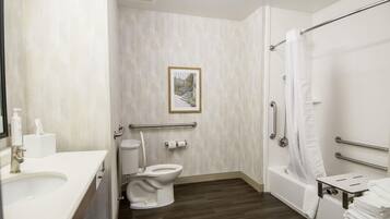 A bathroom with a toilet, bidet, and bathtub. There is a handrail and a picture on the wall.