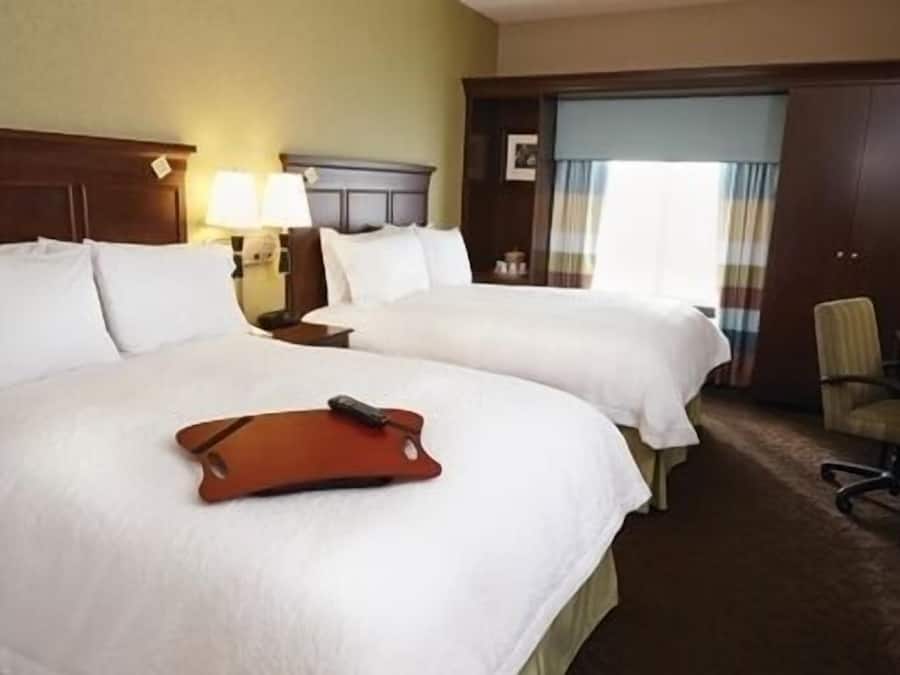 Une chambre d’hôtel avec deux grands lits, un bureau avec une lampe, une chaise et une fenêtre avec des rideaux.