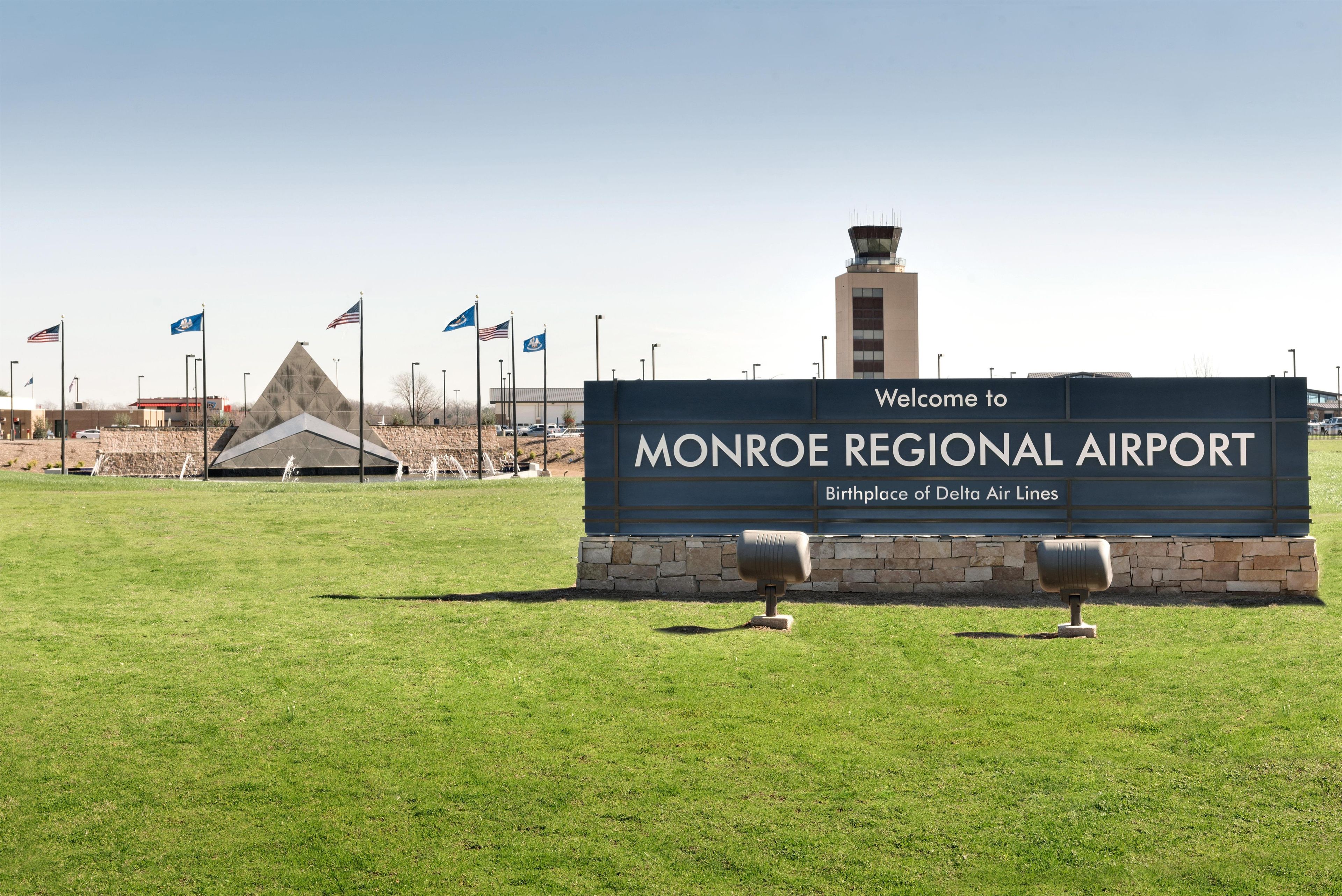 A sign welcoming visitors to Monroe Regional Airport, Birthplace of Delta Air Lines, with a clear sky and a grassy area in the foreground.