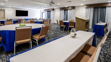 A conference room with tables and chairs, a podium, and a large screen.