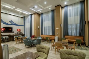 A hotel lobby with seating arrangements, a TV, and a decorative wall.