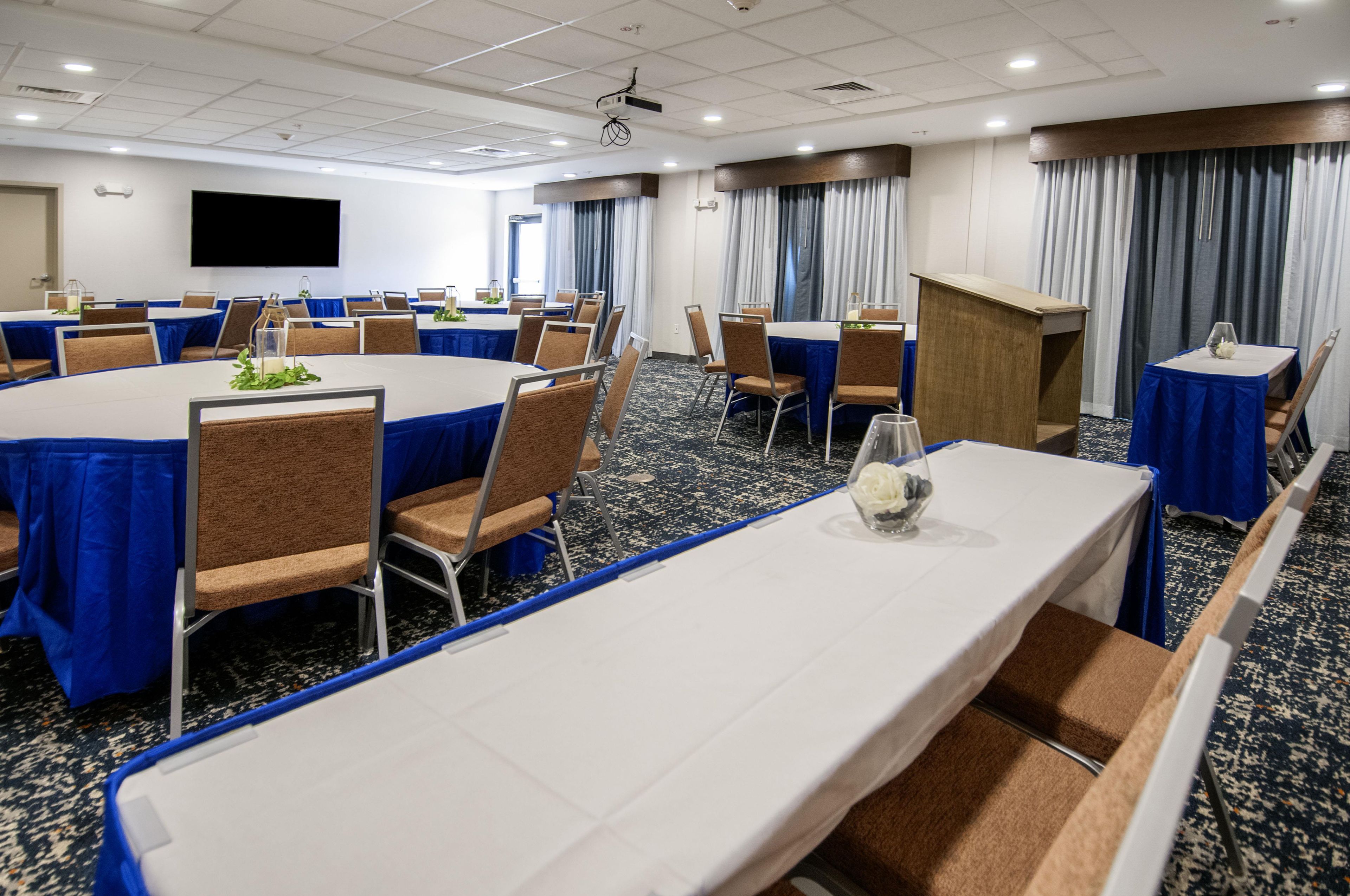 Une salle de conférence équipée de tables et de chaises, d’un pupitre et d’un grand écran.