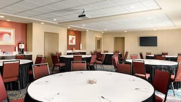 Une salle de conférence dotée de plusieurs tables et chaises, et équipée d’un projecteur et d’un téléviseur à écran plat.