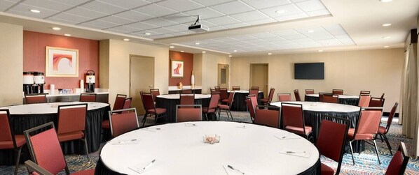 Une salle de conférence dotée de plusieurs tables et chaises, et équipée d’un projecteur et d’un téléviseur à écran plat.