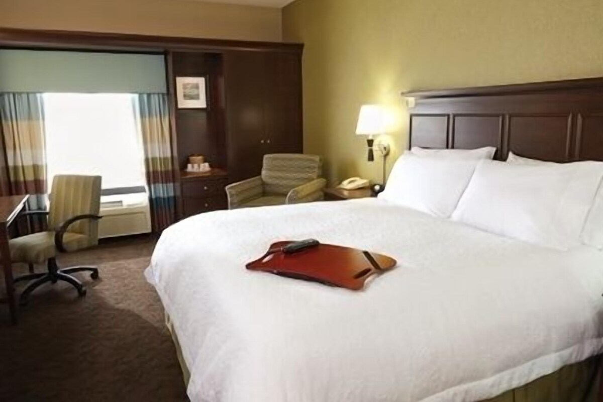 A hotel room with a large bed, a desk, a chair, and a nightstand with a lamp.