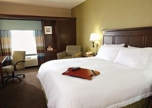 Une chambre d’hôtel avec un grand lit, un bureau, une chaise et une table de chevet avec une lampe.