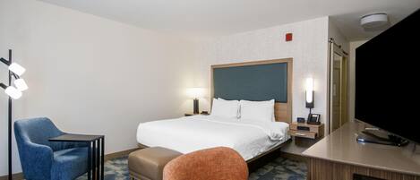 A hotel room with a bed, a desk, a chair, a TV, and a lamp.