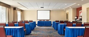 Une salle de conférence avec des rangées de tables, des chaises, un écran de projection et un sol recouvert de moquette.