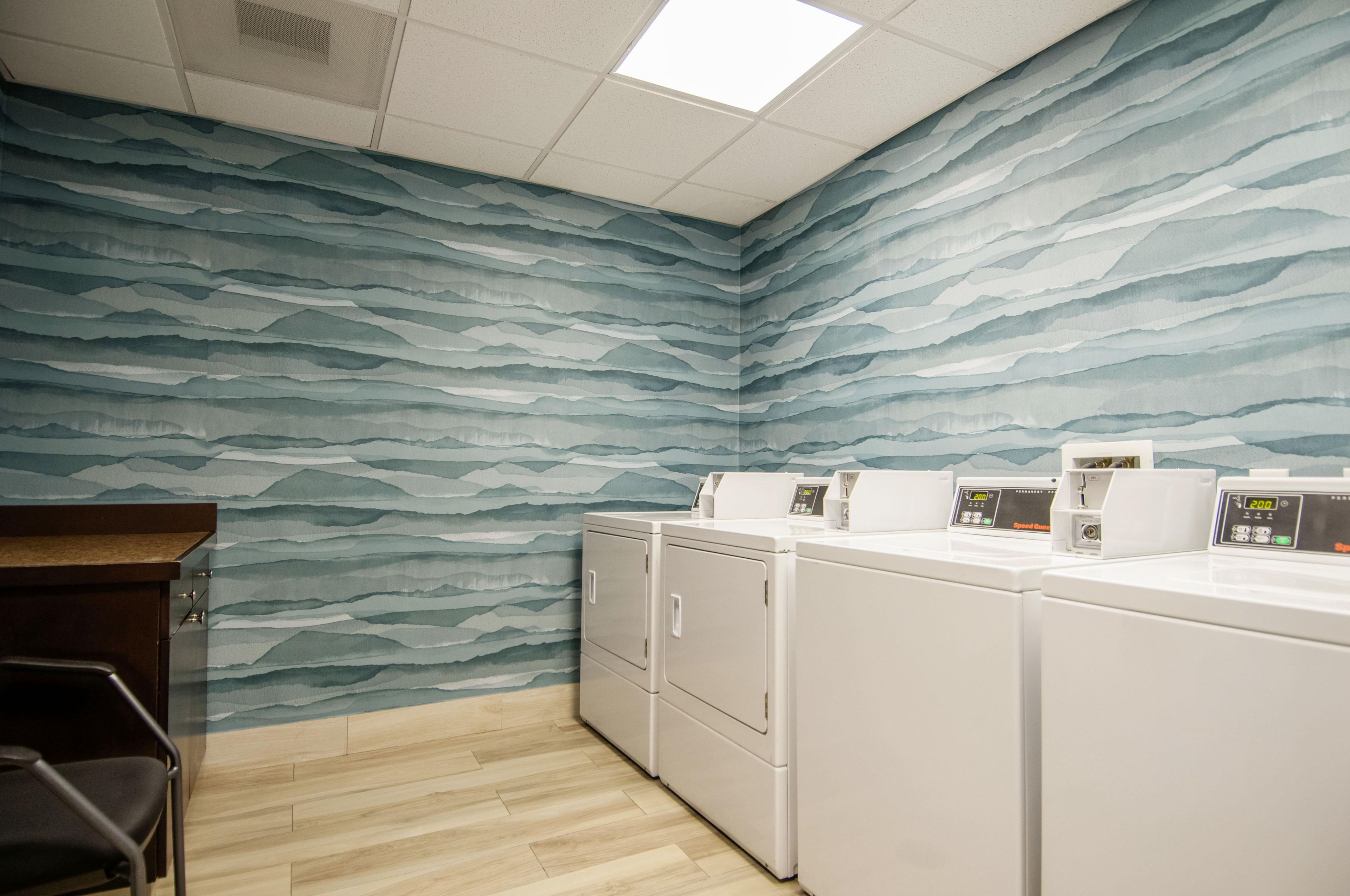A laundry room with a wave-patterned wall, a wooden floor, and stacked laundry machines.
