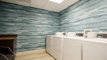 A laundry room with a wave-patterned wall, a wooden floor, and stacked laundry machines.