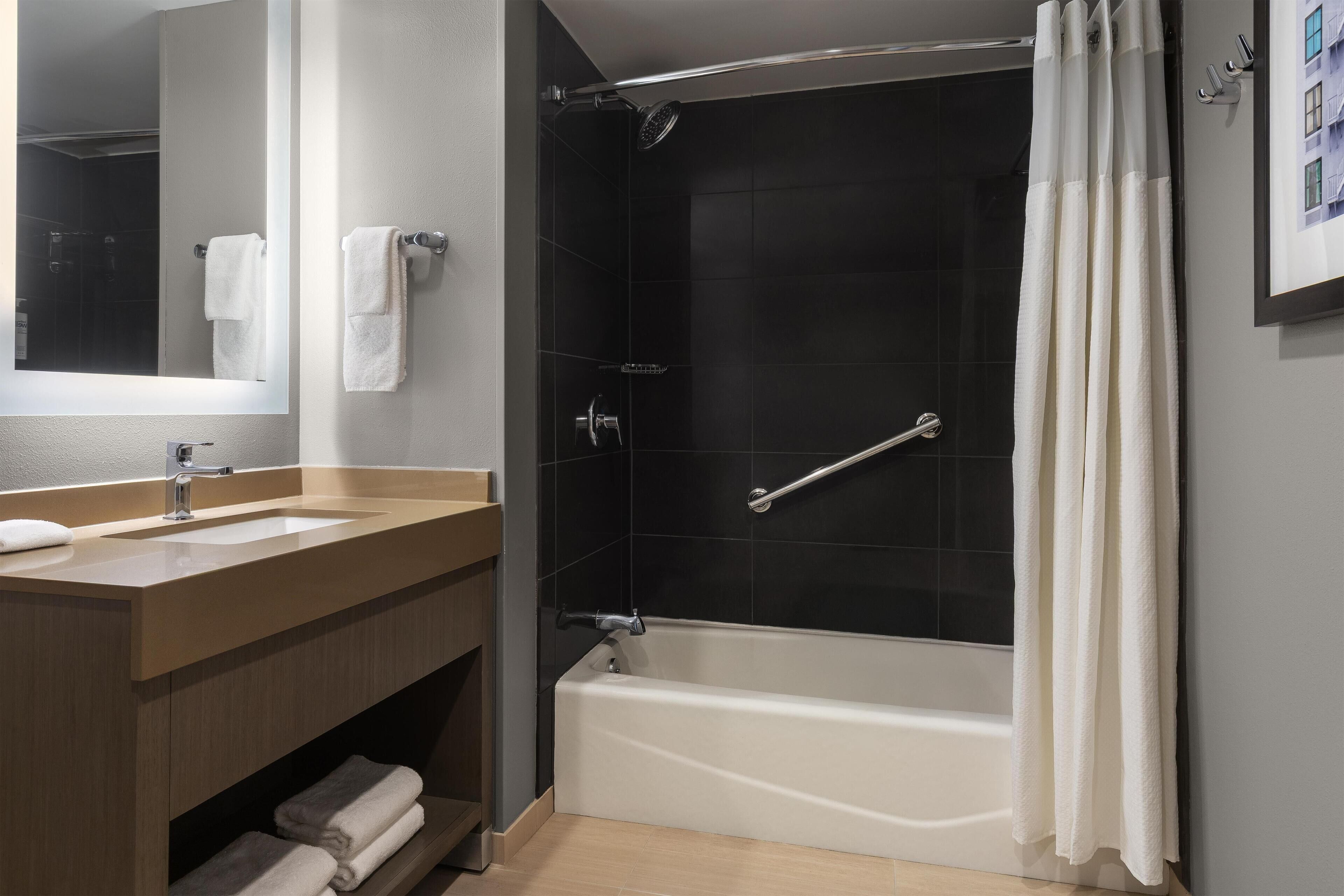 A modern bathroom with a bathtub, a shower, a vanity with a sink, and a mirror.