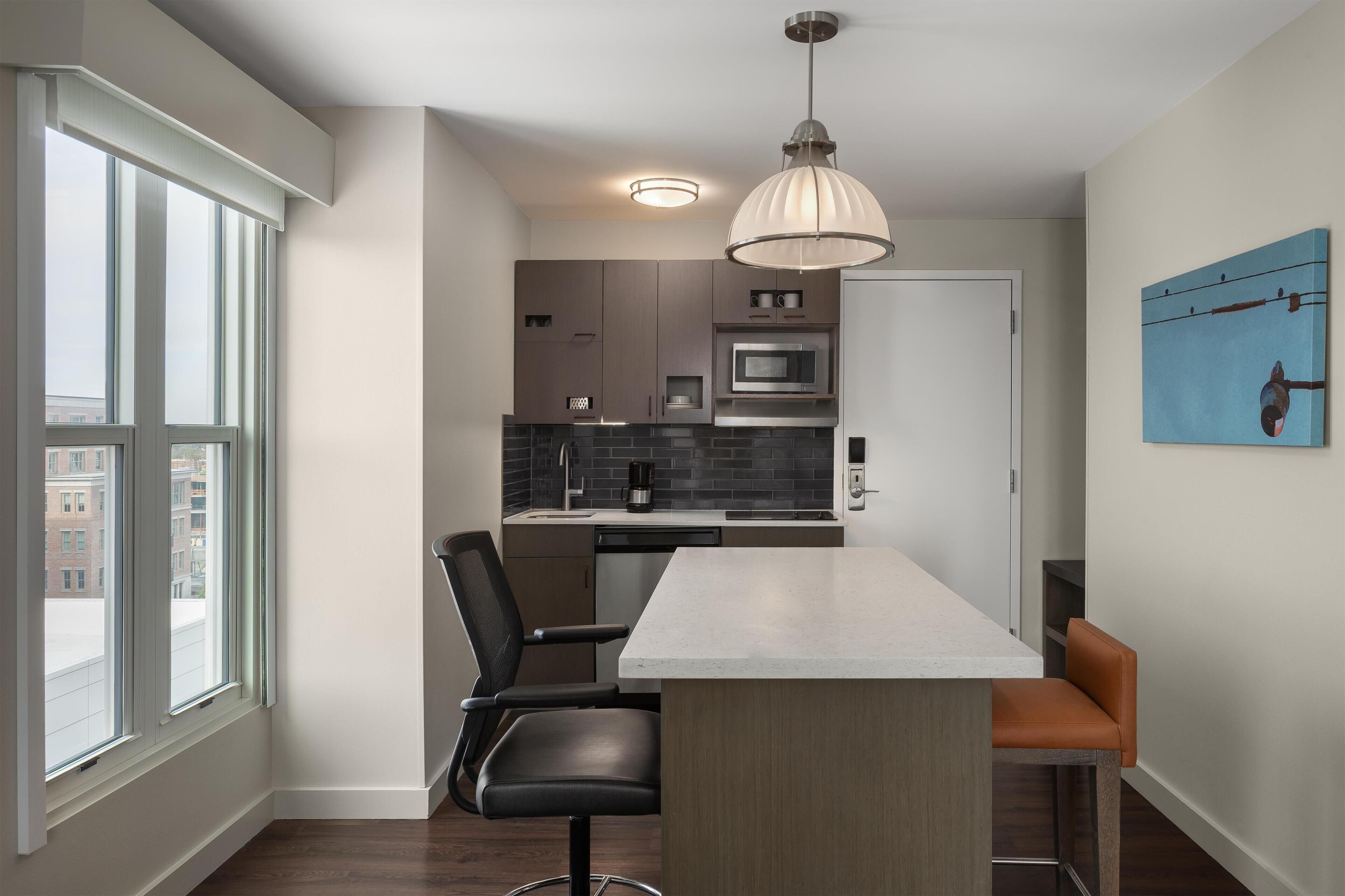 A modern kitchen with a central island, a dining area with chairs, and a large window.