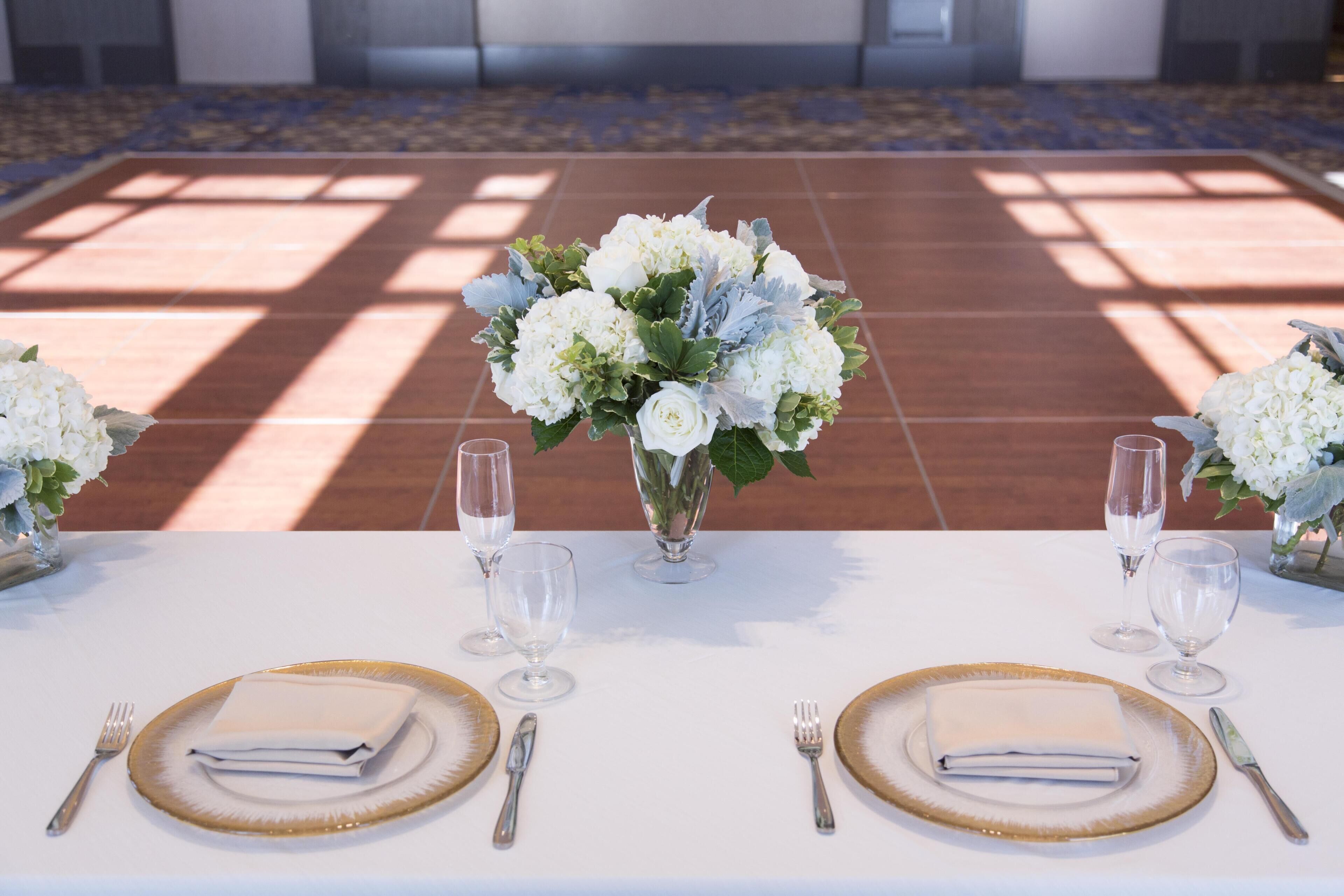 Mesa lista para dos personas con servilletas blancas, platos con borde dorado y copas de cristal.
