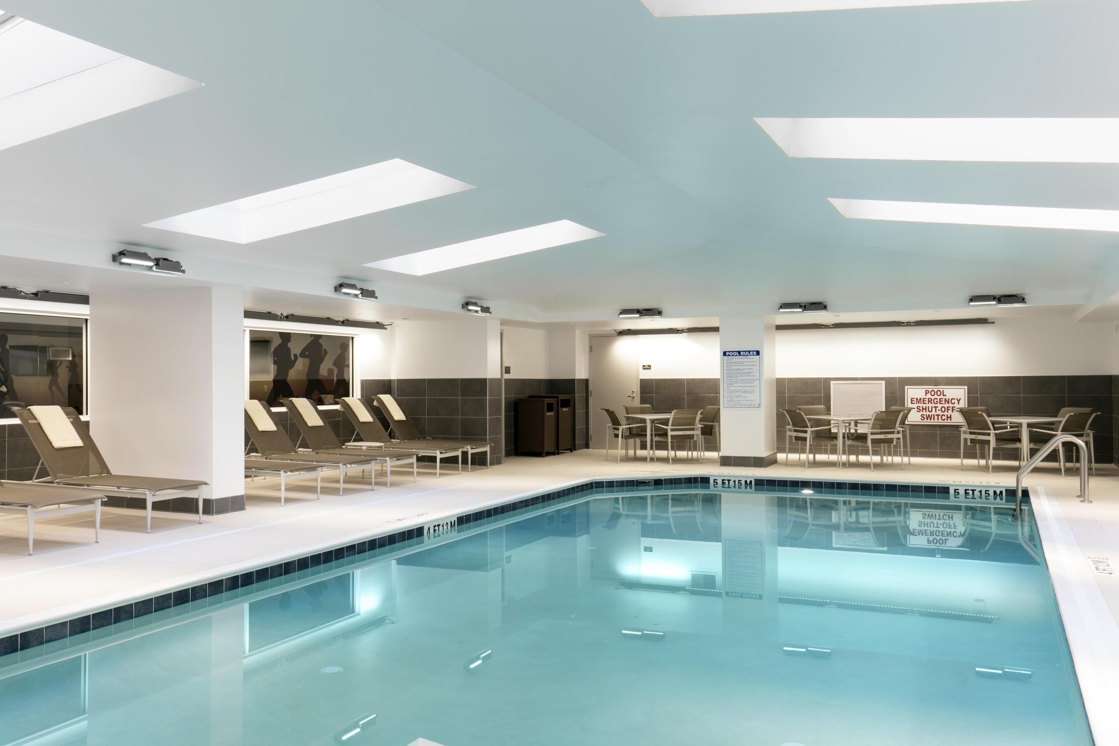 A swimming pool with lounge chairs, a table, and a sign indicating a pool emergency shut-off switch.