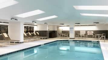 Una piscina con sillas de descanso, una mesa y un cartel que indica el interruptor de corte de emergencia de la piscina.