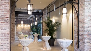 A spacious indoor area with brick walls, multiple tables with white tablecloths, hanging lantern-style lights, and potted plants. - Hyatt House Charleston/Historic District (Charleston)