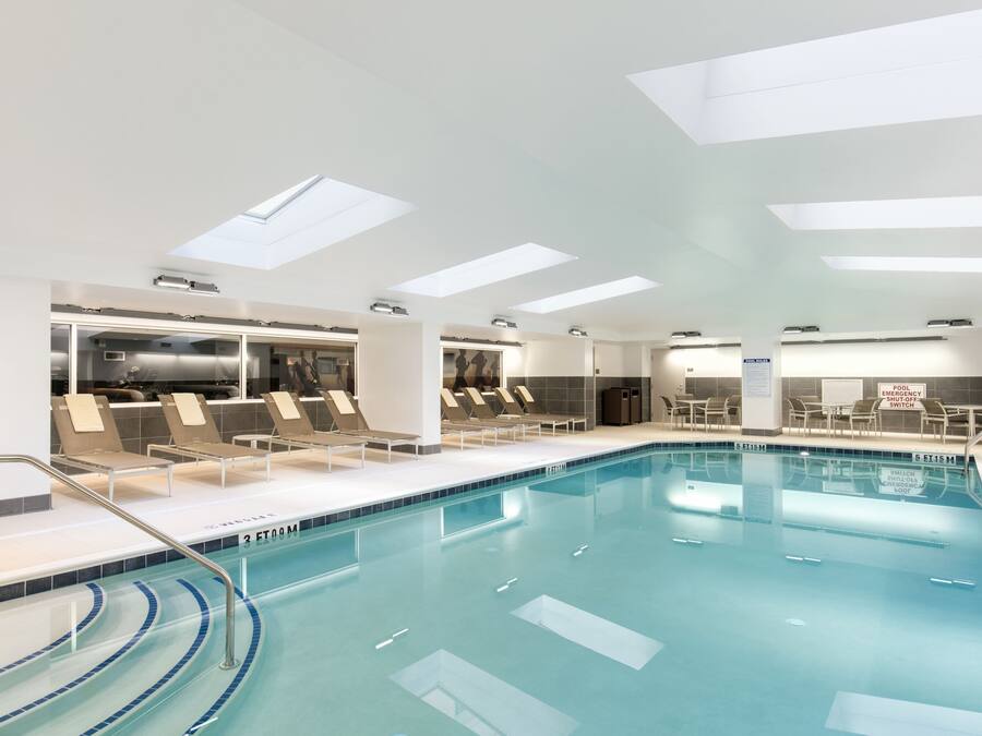 Una piscina interior moderna con agua cristalina, iluminación a través de tragaluces y sillones de descanso a su borde.