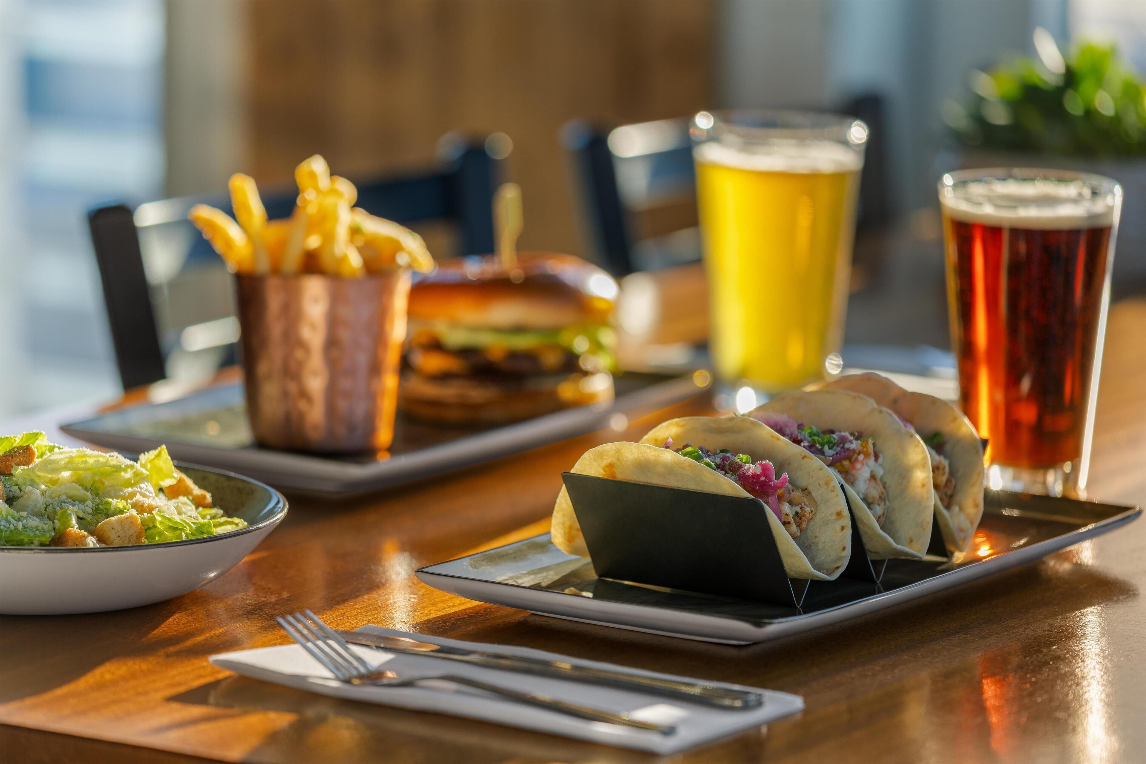 A meal with tacos, fries, a burger, and a salad on a wooden table.